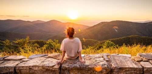 A female traveler overlooking the Blue Ridge Mountains as the sun goes down behind the mountain line.