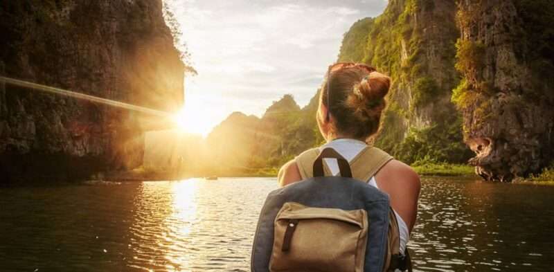 A woman sits at the front of boat with her back turned. She stares through the opening of the Karst mountains.